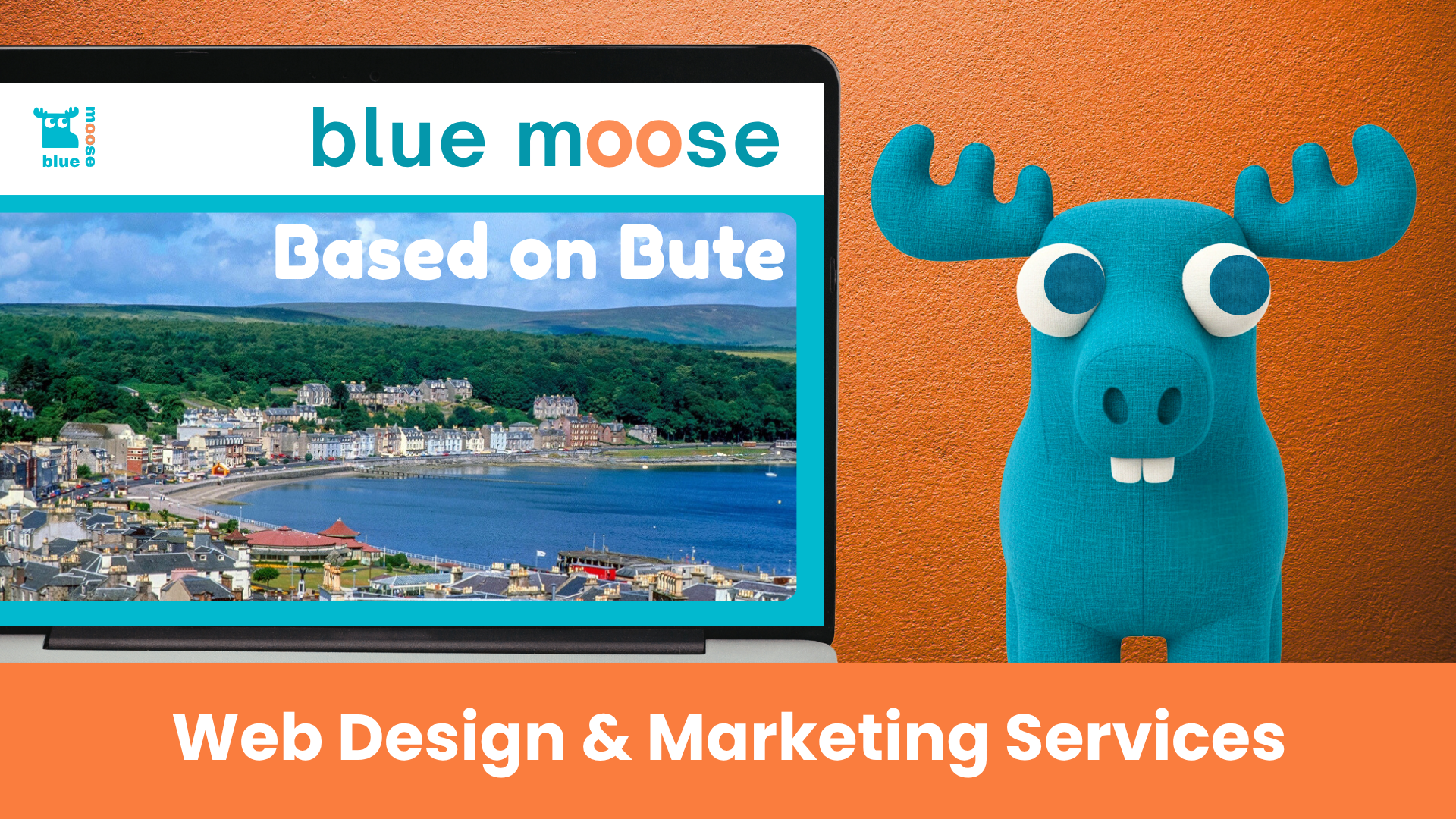 A blue moose plushie sits beside a laptop